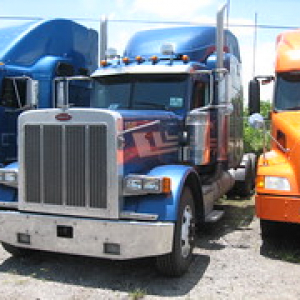 two blue and one orange semi truck lined up in a row