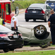 police attending to a flipped over silver car on side of road